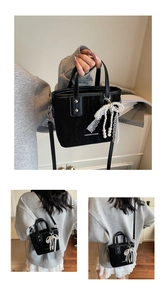 Detail of black textured bucket bag with white fashion text and a lace pearl pendant