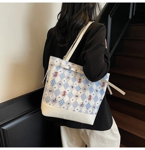 Detail of blue and white quilted tote bag with red bear embroidery and leather strap