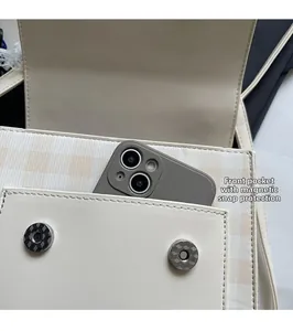 Detail view of plaid shoulder bag with front pocket and dual magnetic snap closure