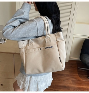 Detail of off-white canvas tote bag featuring blue embroidery and convenient side pocket