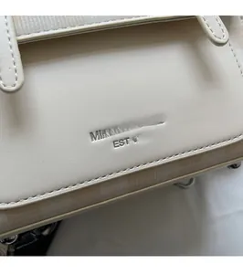 Detailed close-up of the silver embossed brand logo on the off-white textured leather bag