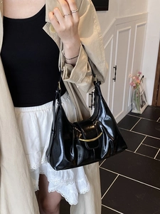 Sac sous le bras noir brillant avec boucle croissant dorée porté par un mannequin