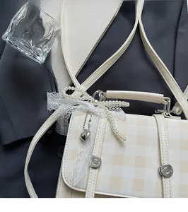Detail of beige checkered crossbody bag with pearl bow and lace ribbons on grey background