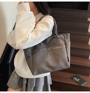 Close-up of grey canvas tote bag with yellow brand embroidery on the front pocket