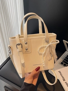 Sac seau blanc crème avec breloque nœud en perles et poignées sur un bureau minimaliste