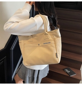 Detail of beige canvas tote bag showing reinforced handles and blue brand embroidery