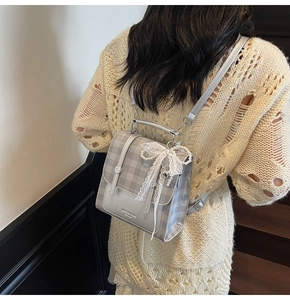 Detail of grey plaid mini backpack featuring lace bow, pearl pendant and metal brand logo