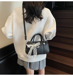 Dettaglio borsa Boston in pelle nera con fiocco in pizzo e pendente in perla