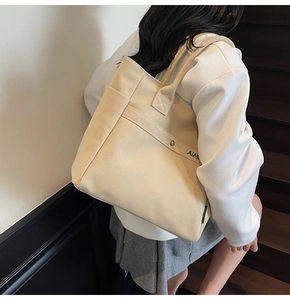 Detail of canvas tote bag showing front pocket with metal snap and wide shoulder strap
