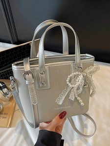 Sac seau argenté texturé avec nœud en perles tenu devant un décor de bureau moderne