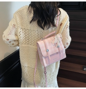 Detail of pink plaid bag with pearl bow charm worn over a cream knit sweater