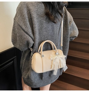 Elegante borsa beige a tracolla con fiocco in pizzo e ciondolo di perle su modella