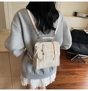 Detail of beige plaid backpack with lace bow and metal heart charm on matte PU leather