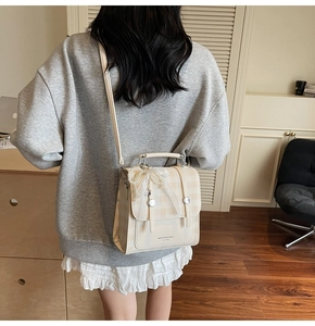 Detail of checkered beige crossbody bag featuring lace pearl bow and logo print
