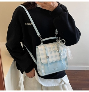Detail of light blue checkered crossbody bag with pearl bow and gold logo accent