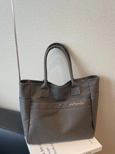 Dark grey canvas tote bag with side pockets and embroidery displayed on white books