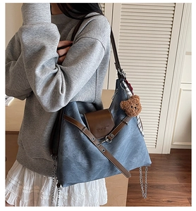 Detail of blue tote bag featuring brown leather flap and silver metal chain tassels