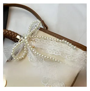 Detail view of pearlescent beige handbag featuring white lace and a pearl bow decoration