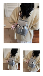 Detail eines silbernen Metallic-Lederrucksacks mit Kettenriemen und Plüsch-Anhänger