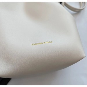 Close-up of white pebble-textured leather bag with golden Fashion & Bags logo engraving