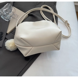 Detail of cream drawstring bucket bag with plush pom-pom charm on grey suit jacket