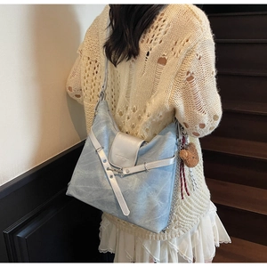 Detail view of denim shoulder bag with brown bear keychain and silver metallic trim