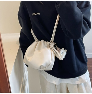 Detail of a beige drawstring bucket bag featuring a white plush sheep doll charm