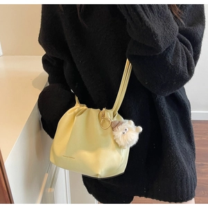 Detail of light yellow drawstring bucket bag featuring soft pleated PU and plush charm