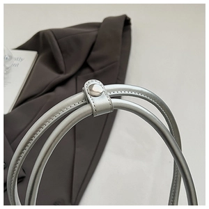 Detailed close-up of the silver metallic handle with snap button on a shell bag