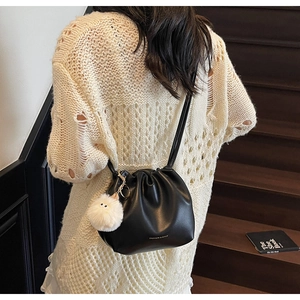 Detail of black drawstring bucket bag with pleats and a cute plush ball charm pendant