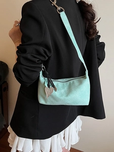 Mint green suede underarm bag with silver heart charm worn by model in black blazer
