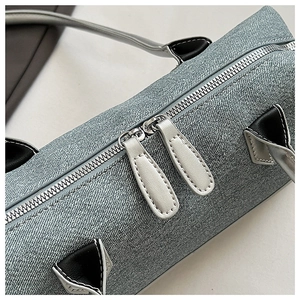 Detail view of denim cylinder bag featuring silver dual zippers and long white leather pulls