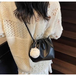 Detail of black drawstring pleated bucket bag with plush charm on model in white outfit