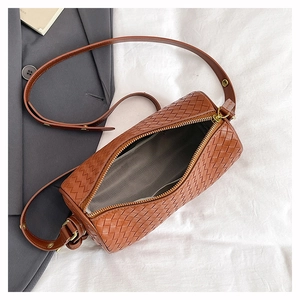 Details einer braunen gewebten Zylindertasche mit Goldreißverschluss und Gurt