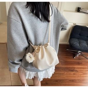 Detail of cream drawstring bucket bag with soft pleated texture and cute plush charm