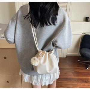 Detail of cream drawstring bucket bag with pleated texture and plush chick charm