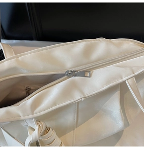 Detalle del cierre de cremallera metálica y bolsillo interior del bolso tote crema