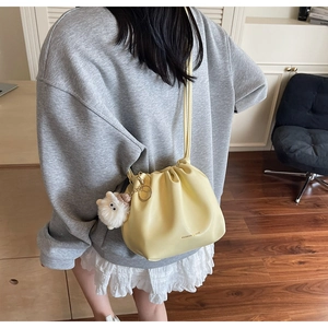 Detail of pale yellow pleated crossbody bucket bag with drawstring and plush sheep charm