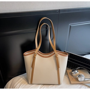 Détail d'un grand sac cabas en cuir crème avec bordure marron à côté d'un ordinateur
