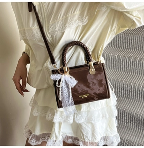 Detailed view of brown leather handbag with marble texture and white lace bow accessory