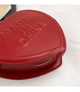 Close-up of heart-shaped red leather bag featuring embossed letters and silver zipper