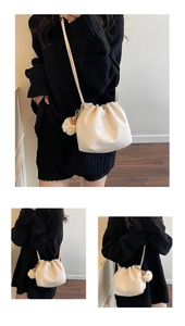 Detail view of cream drawstring bucket bag with soft leather pleats and plush pompom charm