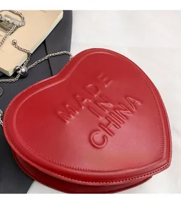 Detail of red heart-shaped crossbody bag with embossed logo and silver chain strap