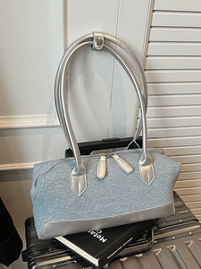 Denim fabric tote bag with long silver straps on a suitcase in a minimalist setting