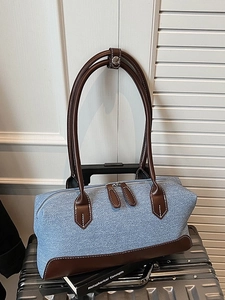 Blue denim shoulder bag with brown leather handles and dual zippers on silver suitcase