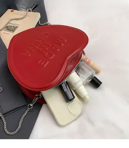 Detail of red heart-shaped crossbody bag with embossed lettering and silver chain strap
