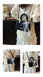 Detail of black glossy handbag with lace bow, pearl pendant and woven handle design