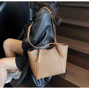 Détail d'un sac cabas en cuir marron caramel avec boucle dorée sur un escalier en bois