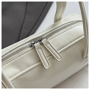 Detail of silver dual zippers and fine stitching on a creamy white leather travel bag