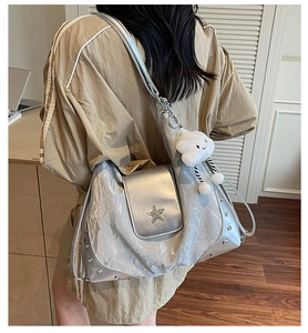 Silberne Schultertasche mit Stern-Detail und Plüsch-Anhänger von einem Model getragen